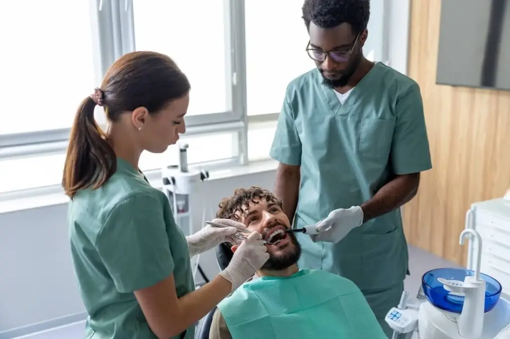 Male dentist with assistant performing orthodontic checkup on patient in modern dental clinic