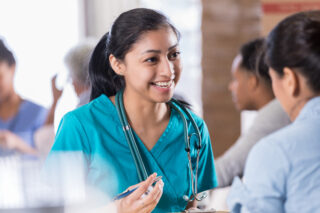 Smiling young Hispanic female healthcare professional talks with mid adult woman about her medical history. The patient is visiting a free medical clinic.